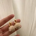 Detail von weißen Plüsch-Ohrringen mit matten Goldreifen, in der Hand gehalten - Creme Pom Pom Gold Creolen Retro