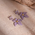 Detailed macro view of matte purple floral earrings with gold center beads on a stone surface - Flower Drop Earrings (Steel Pin) / Purple