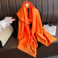 Detail of vibrant orange satin scarf draped over clothes with silky texture and soft sheen - Orange