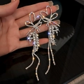 Silver U-shaped tassel earrings with rhinestones and pearls held by hand against black - Silver Heart Wheat Tassel (Silver Earring Post)