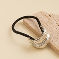 Macro shot of hammered silver metal ornament on a high-elastic black hair tie - Lava Hammered Double Layer Hair Tie / Silver