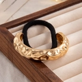 Golden irregular hammered metal pendant with black elastic ponytail holder on tray - Gold-Textured Irregular