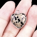 Dalmatian jasper heart pendant with silver bezel frame held by hand on black background - Dalmatian Jasper Silver Edging