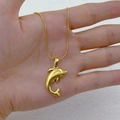 Collana con ciondolo a delfino dorato e catena a serpente mostrata sulla mano - Delfino