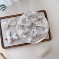 Dettaglio di uno scrunchie in cotone a fiori beige e blu su un piatto di ceramica bianca - Bianco Con Piccoli Fiori Blu Notte