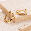 Macro shot of gold C-shaped twisted pearl earrings on a light textured stone background - Gold