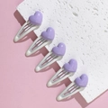 Close-up of five purple heart-shaped BB hair clips on a pink and white textured surface - Purple