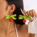Dettaglio di orecchini natalizi a fiocco con perline rosse indossati da una modella - Stile Nastro Verde con Frutto della Mela Rossa
