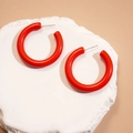 Close-up of bright red C-shaped hoop earrings on a textured white stone surface - Red