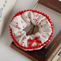 Weißes Haargummi mit Kirschmuster, roter Schleife und Bommeln auf einem Holzbuch - Kirschrot Rand Scrunchie