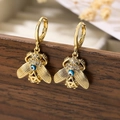 Vergoldete Bienenohrringe mit Evil-Eye-Motiv und Kristallbesatz auf Holzbox - Bienen Stil / Gold