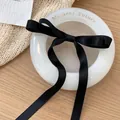 Eleganter schwarzer Satin-Haarclip mit langen Bändern auf einer weißen Schale - Schwarz