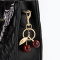 Vue détaillée d'un porte-clés cerise rouge attaché à un sac matelassé noir élégant - Imprimé Léopard Rouge