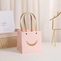Pink paper gift bag with smiley face cutout and brown rope handles on white table - Smiley Pink 10x10x10cm