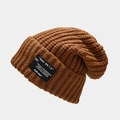 Detailed close-up of thick caramel knit texture and black letter patch on the beanie - One Size / Caramel color