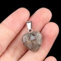 Pendentif cœur en agate naturelle à texture gris-brun tenu entre les doigts - Jaspe Océan