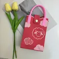Close-up of red knitted phone bag with white lamb pattern and pink handle detail - Little Lamb Pink