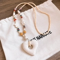 Detail of white porous heart pendant with woven beads on a rustic wooden surface - White Heart