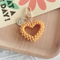 Detail of yellow handmade beaded heart keychain with engraved alloy tag on wooden tray - Yellow