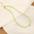 Macro shot of light green beaded necklace with gold Evil Eye heart pendant on marble disk - Green Heart Evil Eye Style
