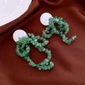 Primer plano de pendientes de piedra verde natural sobre un fondo de seda oscura - Colgante de piedra artificial verde con pasador de plata / Verde