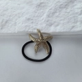 Dettaglio di un ciondolo a stella marina dorata su un elastico nero per capelli elastico - Stile stella marina a spirale dorata