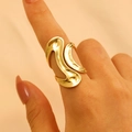 Detail of a wavy gold stainless steel irregular ring worn on finger against soft fabric - 18K Gold Liquid Wave (WG-0337)