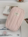 Detailed view of pink quilted fabric texture and beige woven label on the vertical storage bag - Pink