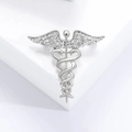 Detalle macro de broche de caduceo plateado con pedrería sobre un soporte blanco - Plateado