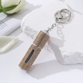 Detail of a golden diamond-studded perfume atomizer with a keychain and white rose decor - Khaki