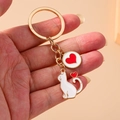 Golden cat keychain with white enamel feline and red heart pendant held in hand - White