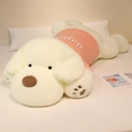 Grosse peluche chien crème avec pull rose Happy posée sur un lit blanc douillet - Blanc perle / 90cm