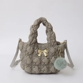 Close-up of quilted grey nylon handbag with golden bow detail and plush ball charm - Tea Green