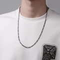 Close-up of a long dark metal Figaro chain necklace worn by a male model over a gray wall - 65cm / Dark Gray