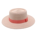Detail of pink straw boater hat featuring a coral red ribbon trim for summer - Pink