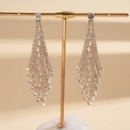 Detalle de aretes largos dorados con flecos y pedrería blanca en soporte de exhibición - Dorado / Dorado