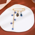 Detail view of a gold safety pin brooch with blue evil eye and Hamsa hand charms - Hamsa Tassel Style (Z85)