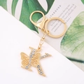 Detail of gold letter K keychain with butterfly design and crystals on a white surface - Letter K