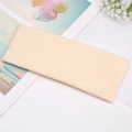 Pale beige ribbed knit wide headband with twisted knot design on a soft beach background - Off-white