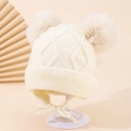 Nahaufnahme einer cremeweißen Baby-Strickmütze mit Ohrenklappen und zwei Bommeln - 1-3 Jahre / Cremeweiß