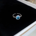 Vista macro del anillo plateado con gema cuadrada azul y piedras brillantes laterales - Anillo-Plata-Azul