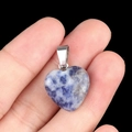 Blue and white natural stone heart pendant with metal loop shown on fingertip - Sodalite