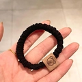 Élastique à cheveux noir avec écusson ours en cuir marron tenu à la main en gros plan - Noir avec étiquette d'ours