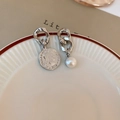 Detail of silver coin and pearl asymmetric earrings on a white ceramic plate - Silver