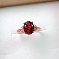 Close-up of an oval-cut red garnet ring in a rose gold setting with leaf-shaped diamond accents - Adjustable Open / Rose Gold