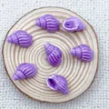 Macro view of purple conch-shaped ceramic beads for DIY jewelry making on wood tray - Purple