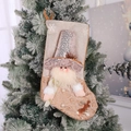 Champagner-goldener Weihnachtsstrumpf mit Pailletten-Wichtel an einem verschneiten Baum - Weihnachtsmann
