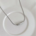 Dettaglio di una collana in argento con ciondolo a barra curva su un piatto di ceramica - Argento