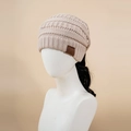 Detail of apricot cable knit ponytail beanie with faux leather tag on a studio mannequin - M (56-58cm) / Beige
