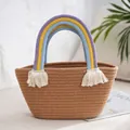 Detail of woven straw handbag featuring a colorful rainbow handle and white cotton tassels - Camel